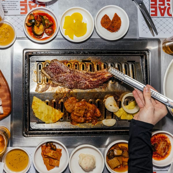 Overhead view of DAE GEE KOREAN BBQ grill with cooking meat, pineapple, onions, and various banchan.