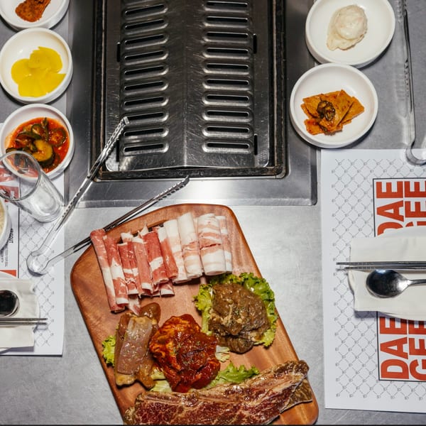 Assorted raw meats and banchan on a table with a built-in grill at DAE GEE KOREAN BBQ.