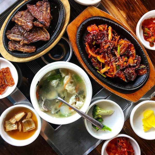 Top-down view of DAE GEE KOREAN BBQ dishes, including grilled ribs, spicy stir-fry, soup, and various banchan.