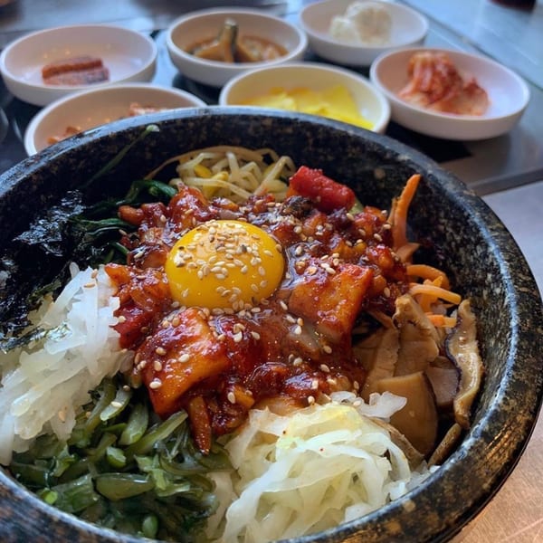 A DAE GEE KOREAN BBQ bibimbap bowl with a raw egg yolk, surrounded by banchan dishes.