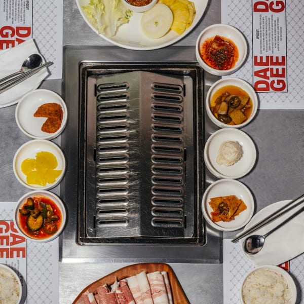 Overhead view of a DAE GEE KOREAN BBQ table with a grill, various banchan, and raw pork belly.